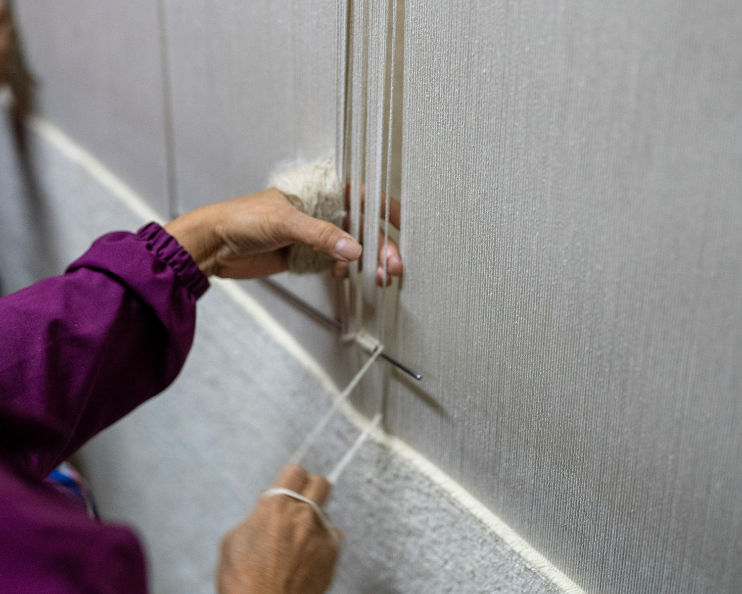 a plain natural wool rug is being hand knotted in Nepal